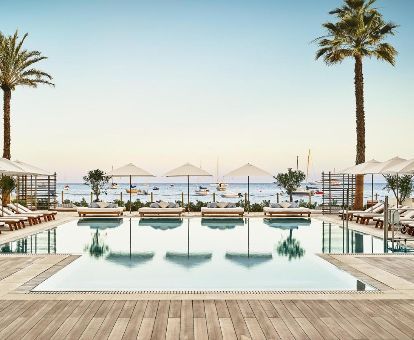 Gran piscina exterior rodeada de tumbonas con vistas al mar de este moderno hotel.