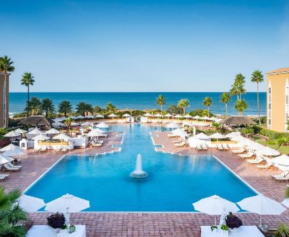 Amplia piscina exterior con mobiliario y vistas al mar de este elegante hotel ideal para parejas.