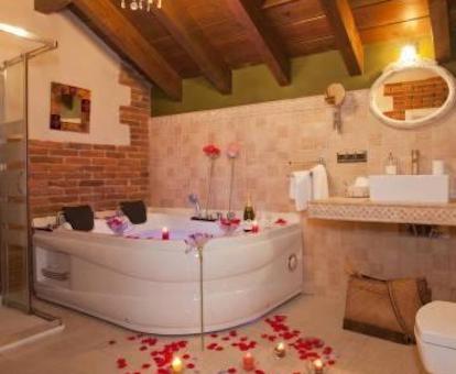 Foto del gran jacuzzi para dos personas con pétalos de rosa en el suelo y dentro en el baño con techo de madera en el apartamento El Aramo