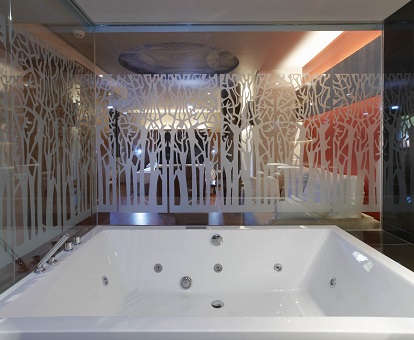 Foto de la bañera de hidromasaje que se encuentra cerca de la cama y detrás de un cristal en la Suite Junior