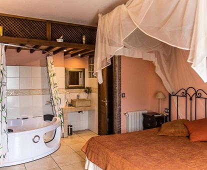 Foto de la Suite con decoración rústica y con vigas de madera donde vemos la bañera de hidromasaje para dos personas que se encuentra muy cerca de la cama.