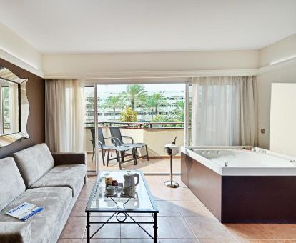 Habitación deluxe con una gran bañera de hidromasaje privada en el salón y terraza con mobiliario y vistas a los jardines del hotel.