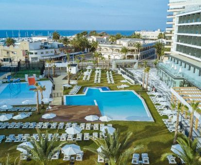Amplia zona exterior con piscinas, jardín y terrazas con mobiliario de este hotel cerca del mar.