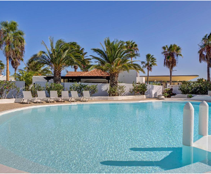 Enorme piscina exterior cercada por hermosas palmeras y chaguaramos. Villa Sávila en Caleta de Fuste