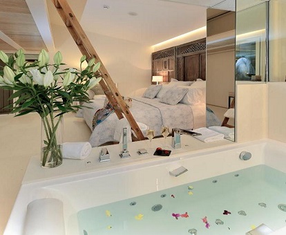 Foto de la Suite Junior donde vemos la bañera de hidromasaje junto a la cama en una bonita habitación muy bien decorada y con un altillo que se accede con escalera ideal para una pareja