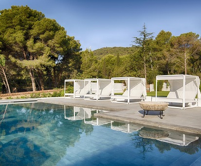 Vista de la piscina con camas balinesas y del entorno natural con pinos en el hotel Eetu