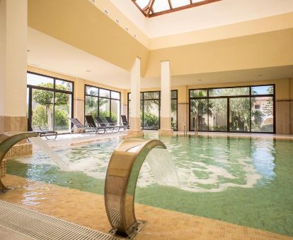 Piscina cubierta con chorros de hidroterapia y vistas al exterior del centro de bienestar del hotel.