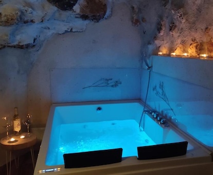 Foto del jacuzzi del apartamento bajo el techo de piedra, con unas velas en el lateral y una mesita con unas copas y una botella de vino