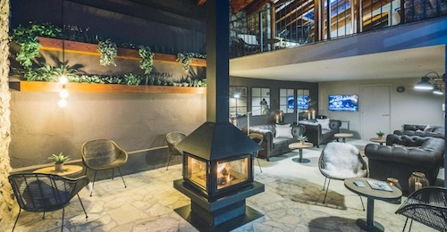 Salon con sillas entorno a una chimenea y unos sillones de cuero para tomar una copa en el salón de Intrepid Hotel Rural