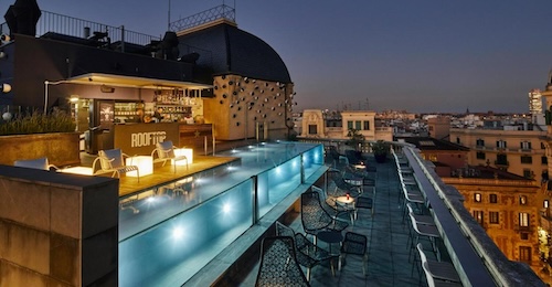 Terraza por la noche con una serie de sillas junto a la piscina y con vistas a la ciudad de Barcelona
