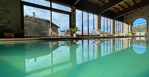 Piscina climatizada bajo un techo de madera, con tumbonas y grandes cristaleras que dan al exterior en el hotel L'Avenc Benestar Rural