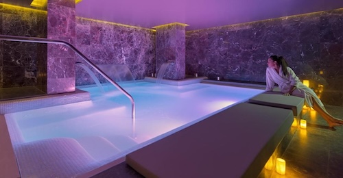 Chica junto a la piscina de cromoterapia del spa con luces naranja en el suelo del hotel The One Barcelona GL
