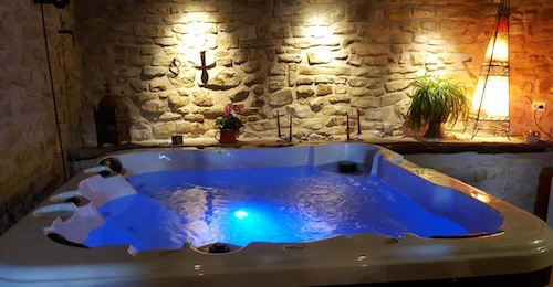 Foto del jacuzzi cuadrado con capacidad para 4 personas con las luces de cromoterapia encendidas y donde se puede ver la pared de piedra al fondo con algunas luces.