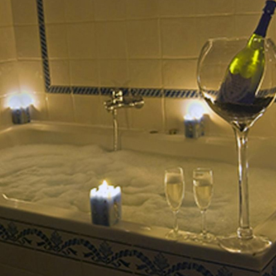 Foto de la bañera de hidromasaje con espuma, velas y una gran copa con una botella de champán en su interior