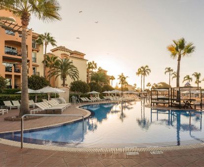 Hotel romántico con una amplia zona exterior con piscina al aire libre rodeada de tumbonas y palmeras.