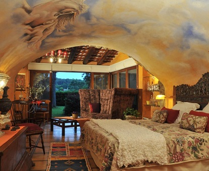 Foto de la habitación con techos decorados y suelos de baldosas también decoradas. Hay una gran cama y al fondo de la habitación se puede ver el jardín del hotel.