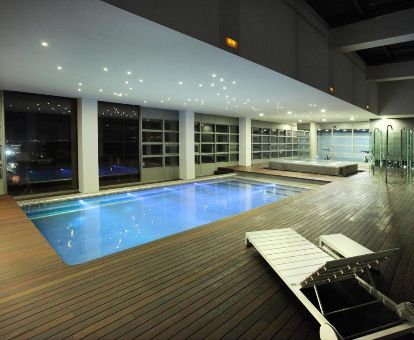 Piscina cubierta con tumbonas y vistas a la ciudad del centro de bienestar del hotel.