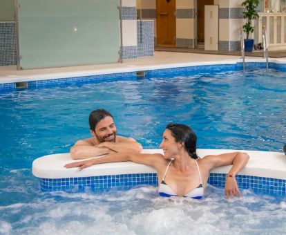 Pareja disfrutando de la piscina con elementos de hidroterapia del spa del hotel.