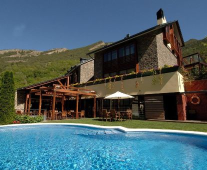 Hermoso hotel rural con amplia piscina exterior rodeado de montañas.