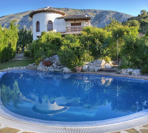 Foto de la piscina circular en el jardín y con la casa de dos plantas rodeada de árboles