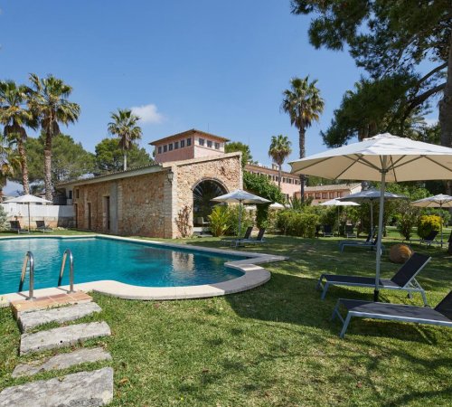 Foto desde la piscina de Virrey Finca Hotel donde vemos las tumbonas bajo la sombrilla en la piscina, y con el chalet de estilo rústico de fondo.