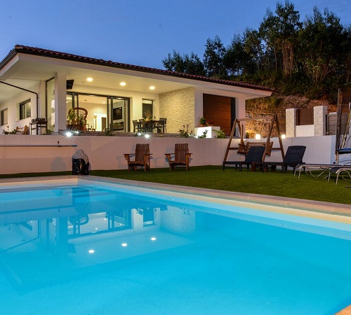 Foto desde la piscina con la Villa Luna con forma modernas y terraza con jardín al fondo.