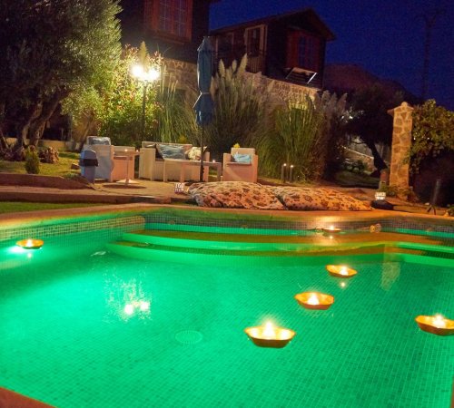 Foto de la piscina de noche con luz de color verde y donde se ven los jardines al fondo y algunas de las cabañas en Cabañas El Descansito