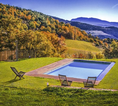 Piscina en Cal Sodhi con tres sillas y rodeada de cesped en pleno jardín y con vistas a las montañas de Argestues
