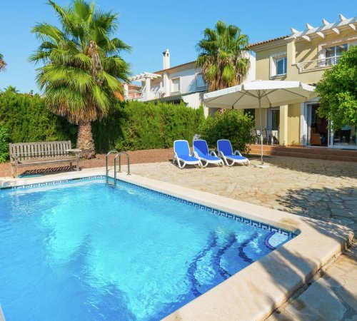 Piscina con unas tumbonas bajo una sombrilla en la terraza frente a la Villa