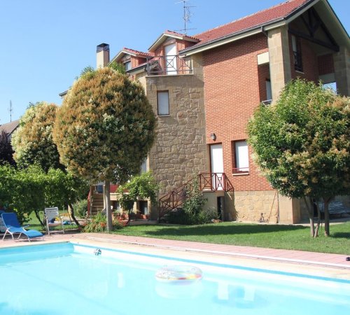 Piscina frente a casa con árboles y jardines