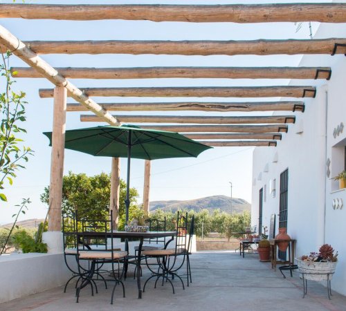 Foto del patio frente a la casa Villa Maria Eusebia con paredes de color blanco donde se ven las mesas bajo una sombrilla