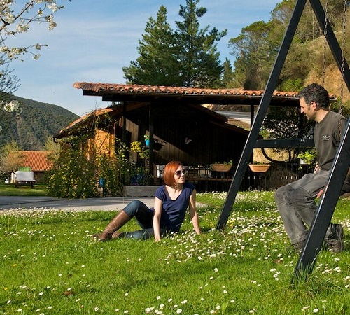 Pareja conversando en la zona de juegos para niños y columpios del jardín de las casa de madera Casa Matapalacios