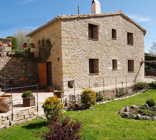 Exterior de la Casa Rural Torre Gargallo donde vemos el jardín, cesped y acabado de piedra y estilo rústico de la casa