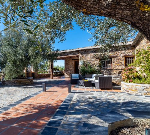 Foto del exterior de Cortijo la Loma de la Alpujarra donde se puede ver los árboles, los jardines y la terraza para disfrutar de las vistas a las Alpujarras