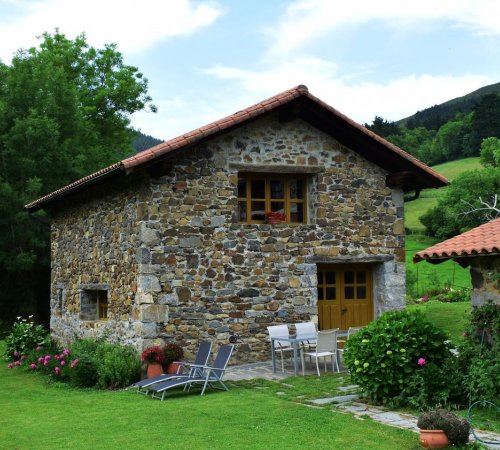 Foto del exterior de la casa Martiamuno donde se ve el estilo rústico de piedra de la casa y los alrededores de naturaleza y prados