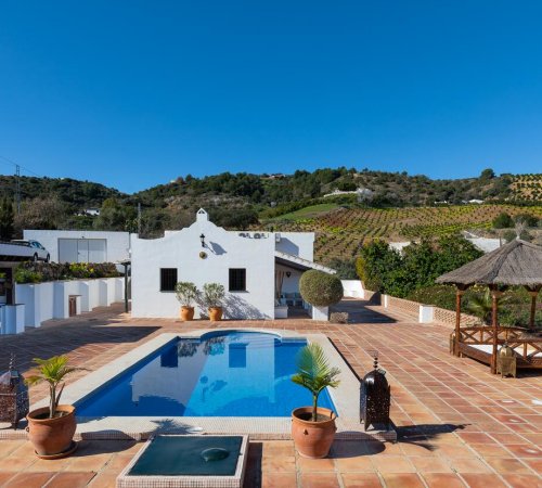 Foto desde la piscina con la Finca Alhaurin Sefardi de color blanco resaltando sobre las colinas y campo malageño al fondo.