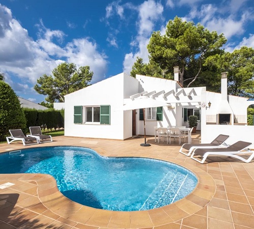 Foto del exterior de Villas Geisan donde se ve la piscina, palmera, árboles y mobiliario para tomar el sol