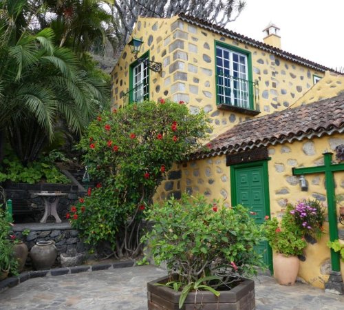 Foto del exterior de Finca Doña Juana con las paredes en color amarillo y las plantas que hay alrededor de la casa