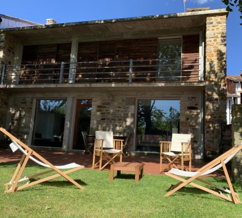 Foto del jardín junto a Casa Otxandi donde se ven dos sillas para tomar el sol en el exterior de la casa de estilo rústico pero con líneas modernas