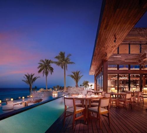 Foto del restaurante con las mesas frente a una piscina alargada con las palmeras y unas tumbonas al fonde en el Nobu Hotel Los Cabos