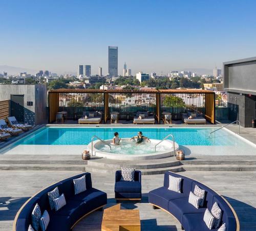 Dos personas en un jacuzzi circular en la terraza del Hilton Guadalajara Midtown con vistas a la ciudad y junto a la piscina con solarium para tomar el sol