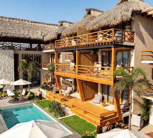 Piscina frente a una bloque de habitaciones con terraza de madera y con mobiliario y hamacas para tomar el sol en hotel Casa Joseph Zicatela - Adults Only