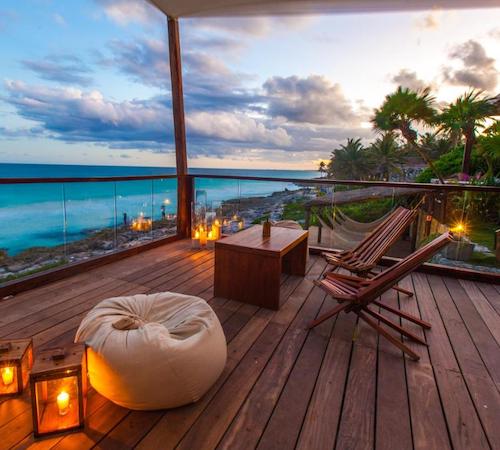 Terraza de suelo de madera con vistas a la selva y a la playa con dos sillas y una tumbona desde la que se contempla el mar en la suite del Mezzanine a Colibri Boutique Hotel - Adults Only