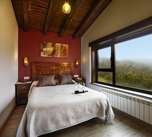 Suite de estilo rústico con un gran ventanal junto a la cama con vistas al campo en el hotel La Tejera Padel en la provincia de Asturias