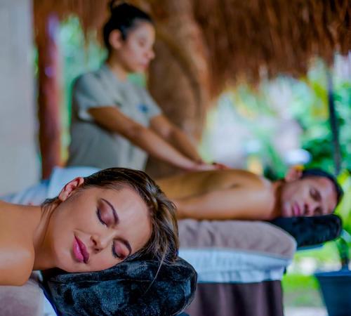 Una mujer tumbada con los ojos cerrados mientras recibe una masaja relajante al mismo tiempo que su pareja que se puede ver al fondo tambiém recibiendo un masaje en el hotel Magic Blue Spa Boutique Hotel Adults Only