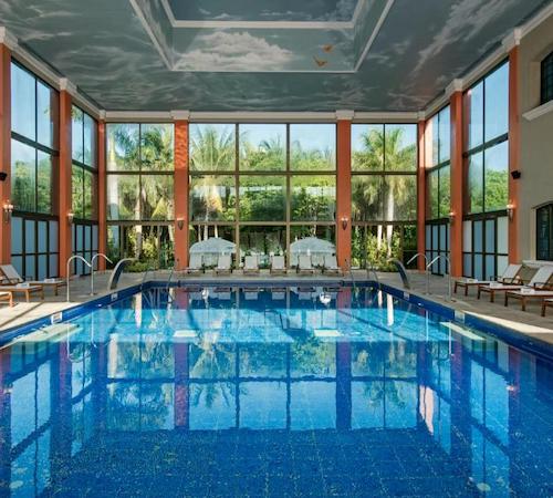 Piscina con una cristalera al fondo con vistas a la selva y una serie de sillas a ambos lados de la piscina en el hotel Iberostar Paraiso Beach