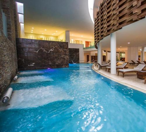 Piscina del SPA en hotel Grand Velas Riviera Maya con camas en el interior de la piscina y otras camas en el borde de la piscina que se extiende hasta el fondo donde se pueden ver los chorros de hidromasaje
