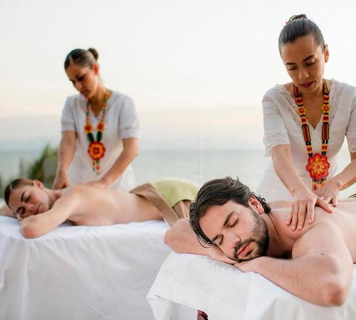 Una pareja tumbados frente al mar mientras dos mujeres les dan un masaje relajante en el hotel resort Grand Velas Riviera Nayarit