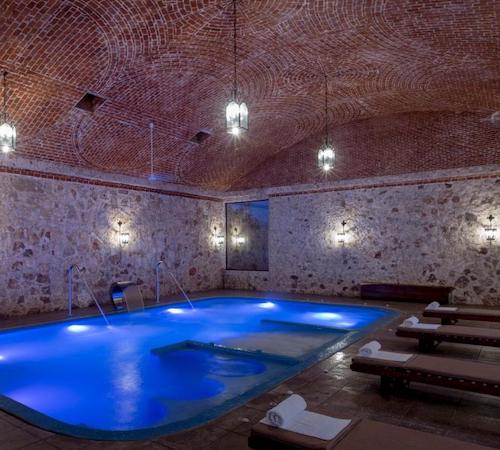 Zona de spa bajo una bóveda de ladrillos y unas camas para recibir masajes al borde de la piscina con chorros de hidromasaje en el hotel Hacienda Santa Cruz Merida