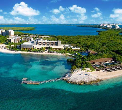 Vista desde el cielo donde se puede ver una serie de hoteles en una playa blanca enfrente de una zona de selva junto a un mar de color turquesa